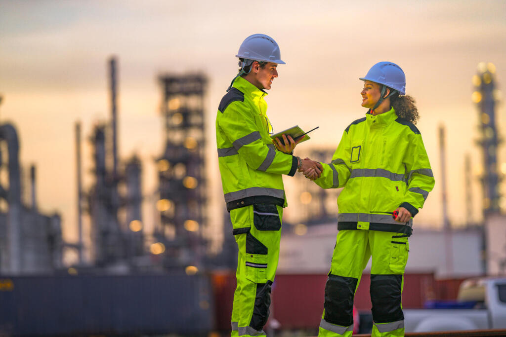 Two industrial workers in high-visibility safety uniforms discus